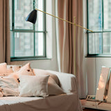 Nala Adjustable Floor Lamp with Marble Base in Matt Black & Gold, shown bedside with its angled gold arm and black dome shade extending over a bed.