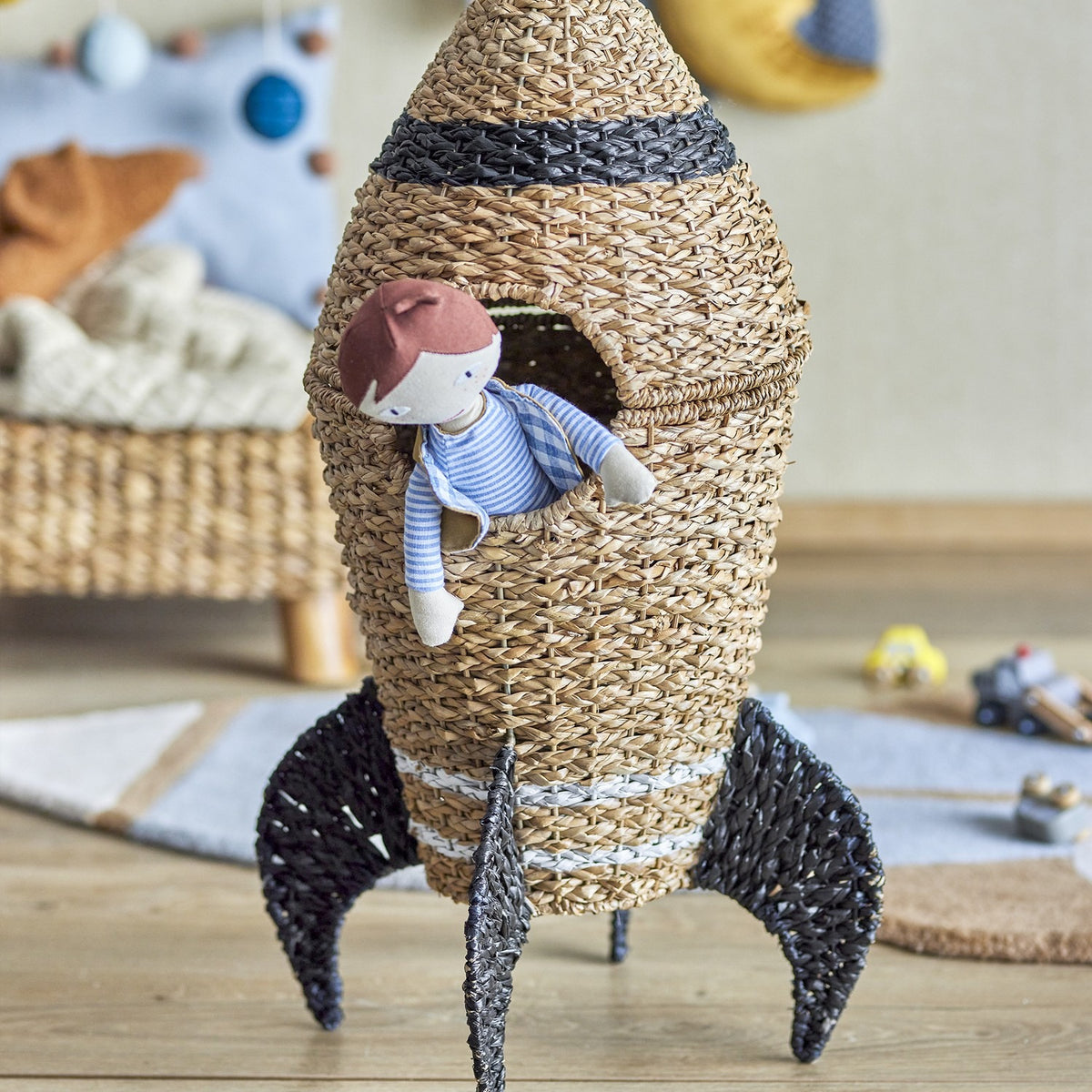 Cosmina Rocket seagrass storage basket in natural weave with black-banded nose cone, shown in a nursery with a doll peeking from the opening.