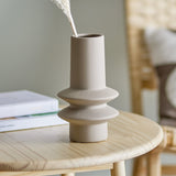 Isold Stoneware Vase 22cm in beige with a slender neck and two flared rings, matt ceramic finish, shown on a wooden side table with dried pampas grass.