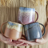 Cloe Speckled Stoneware Mugs, set of 3, 400ml, each with streaked glaze fading into a speckled lower body in pink, terracotta and blue-grey, held in cupped hands.