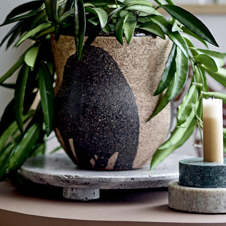 Nala Terracotta Plant Pot in Black with hand-painted leaf-like strokes, holding a green leafy plant on a stone tray beside a lit candle on marble holders.