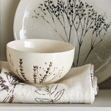 Bea Floral Stoneware Bowl 11.5cm in beige with sprig floral motif, plain cream interior, shown beside a patterned plate and floral linen napkin.