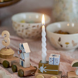 Lit white twist candle from the Twist Candles Pack of 12 in a wooden toy train holder with gift box detail, set among bowls on a table.