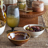 Heikki Floral Stoneware Bowl 12cm in amber-brown, shown filled with sauce and styled with a white olive bowl and glassware on a dining table.
