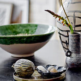 Moez Stoneware Bowl 30cm in Green with glossy rim glaze, shown on a dark table beside a decorative vase and ceramic trinket dish.