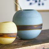 Melike Striped Glass Vase 18.5cm in Blue, a round matte glass vase with a dark organic band at its centre, shown beside a smaller yellow version on a wooden shelf.