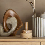 Esad Resin Ornament in brown, two interlocking sculpted loops with a speckled finish, displayed on a sideboard beside a candle holder and ribbed vase.