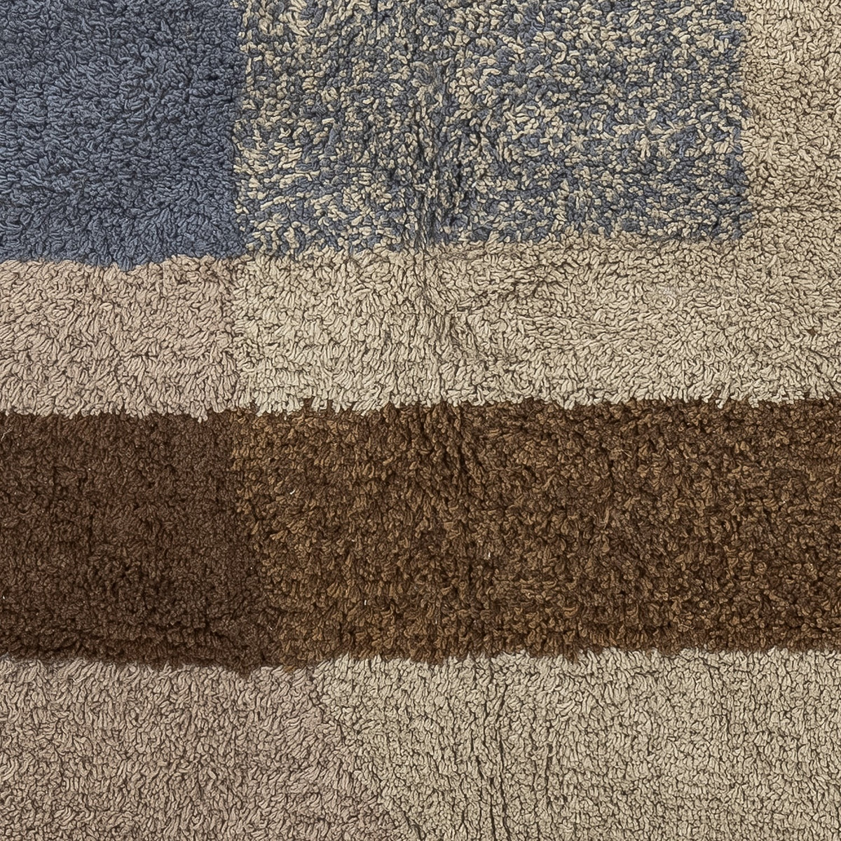 Close-up of the Zofia tufted cotton rug in beige, showing a deep shaggy pile with blue-grey and brown geometric blocks in solid and speckled tones.