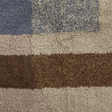 Close-up of the Zofia tufted cotton rug in beige, showing a deep shaggy pile with blue-grey and brown geometric blocks in solid and speckled tones.