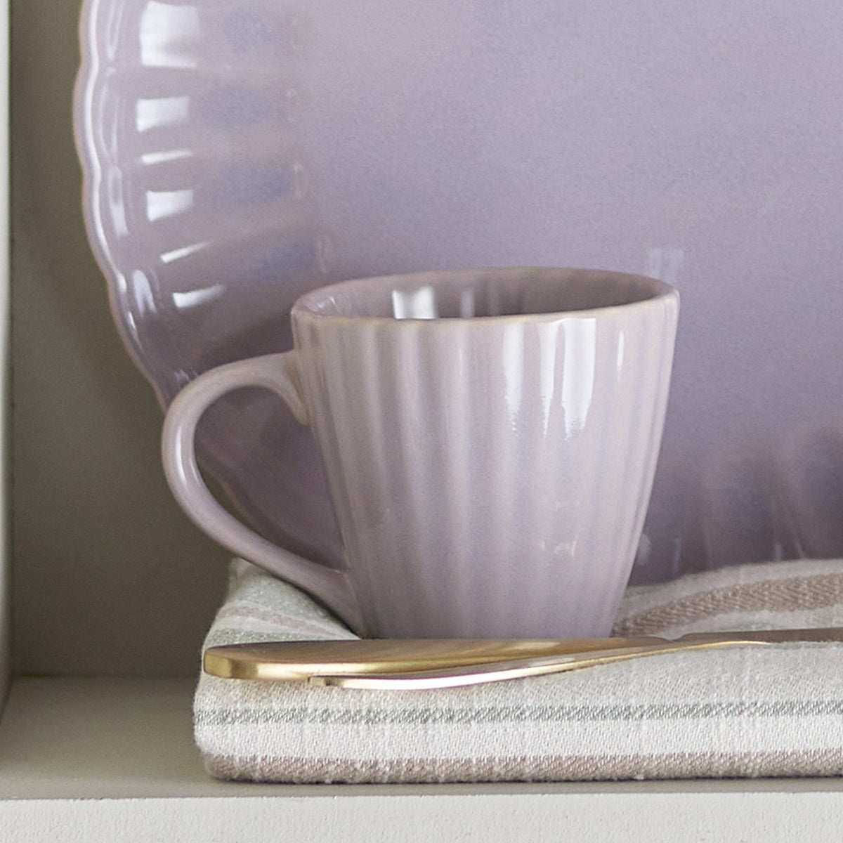 Latina Fluted Stoneware Cup 220ml in pink with ridged texture and loop handle, shown on a striped cloth with a matching scalloped-edge plate and gold-trimmed knife.
