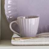 Latina Fluted Stoneware Cup 220ml in pink with ridged texture and loop handle, shown on a striped cloth with a matching scalloped-edge plate and gold-trimmed knife.