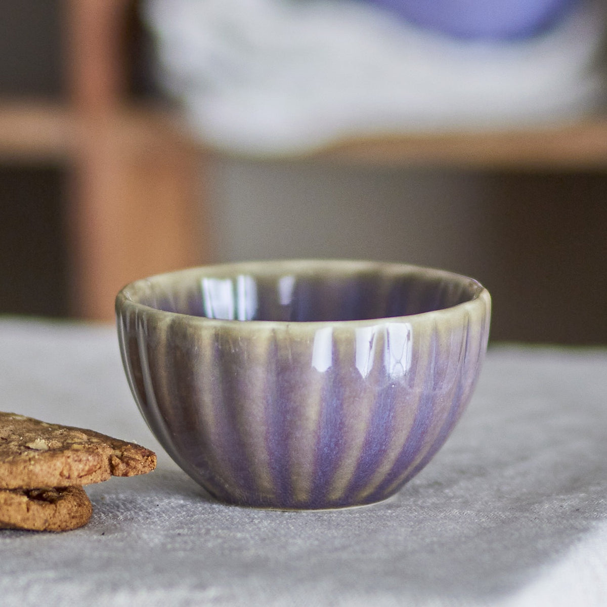 Latina Stoneware Bowl 9cm in grey with fluted ribbed sides and glossy glaze, shown beside oatmeal biscuits on a linen surface.