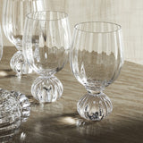 Taurin Round Wine Glass in clear ribbed glass with a short round footed base, shown in a set on a marble-topped table.