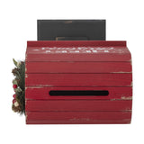 Red distressed MDF Christmas postbox with curved slatted roof, letter slot, Merry Christmas script, and a pine cone and berry wreath accent, shown on a white background.