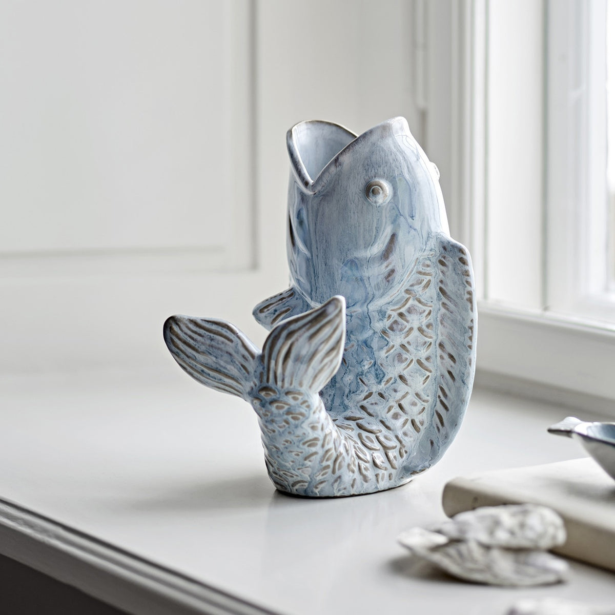 Hiro Fish Stoneware Vase 21cm in blue, shaped like a leaping fish with open mouth as the neck, scaled body and curled fanned tail, displayed on a windowsill.