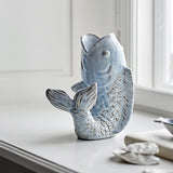 Hiro Fish Stoneware Vase 21cm in blue, shaped like a leaping fish with open mouth as the neck, scaled body and curled fanned tail, displayed on a windowsill.