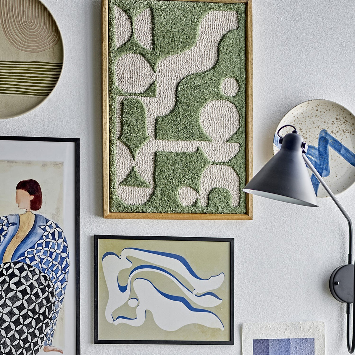Longton Wool Wall Decor in Green, a tufted textile wall art piece with abstract shapes in a slim wooden frame, shown in a gallery wall with other framed art and a wall lamp.