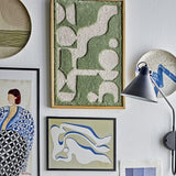 Longton Wool Wall Decor in Green, a tufted textile wall art piece with abstract shapes in a slim wooden frame, shown in a gallery wall with other framed art and a wall lamp.