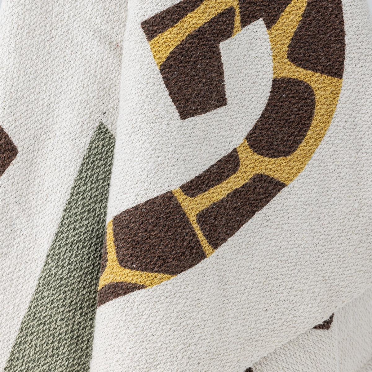 Close-up of the Memmo Cotton Throw in multi, showing a knitted cream ground with a bold letter in giraffe-print mustard and brown, beside an olive green shape.