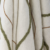 Osasio Cotton Throw in cream, close-up of the slubby woven cotton with tufted sage-green loop stitching and fine tan embroidered lines in sweeping curves.