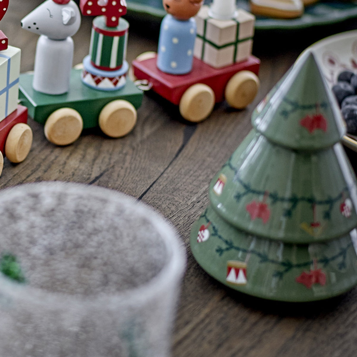 Yule stoneware Christmas decorations set of 2 in green, tiered tree shapes with painted fir garlands and ornament details, shown on a wooden table beside wooden toy figures.