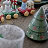 Yule stoneware Christmas decorations set of 2 in green, tiered tree shapes with painted fir garlands and ornament details, shown on a wooden table beside wooden toy figures.