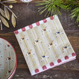Folded Merry-go-round Christmas napkin with carousel horse print and scalloped red-and-white canopy, shown on a wooden table with a matching plate and pine branches.