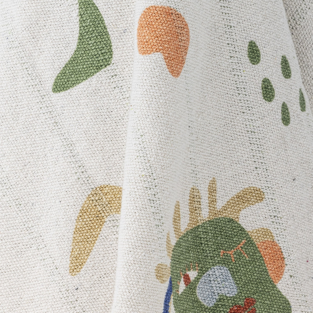 Sylvie Cotton Throw close-up in multicoloured fabric, showing abstract shapes including a sleepy-faced figure, dots, squiggles and curves in green, orange, blue and mustard tones.