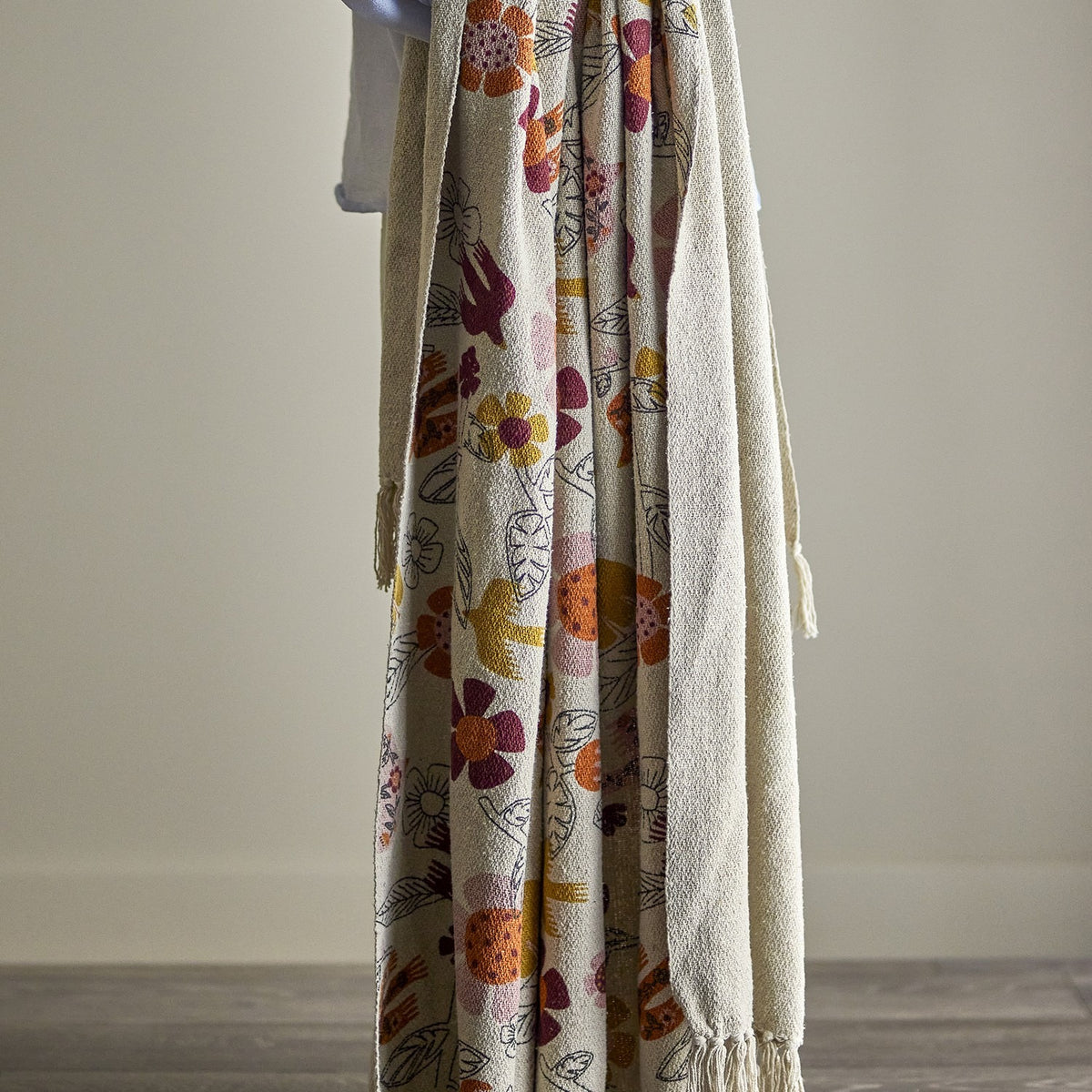 Vivielle Floral Throw in multicoloured cotton-blend fabric, draped in folds showing a printed pattern of flowers, leaves and birds with fringed edges, against a plain neutral background.