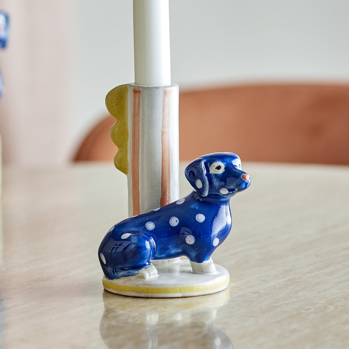 Dachsy Dog Stoneware Candle Holder in multicoloured ceramic, a polka-dot dachshund beside a striped candle tube with a scalloped fin, shown on a tabletop.
