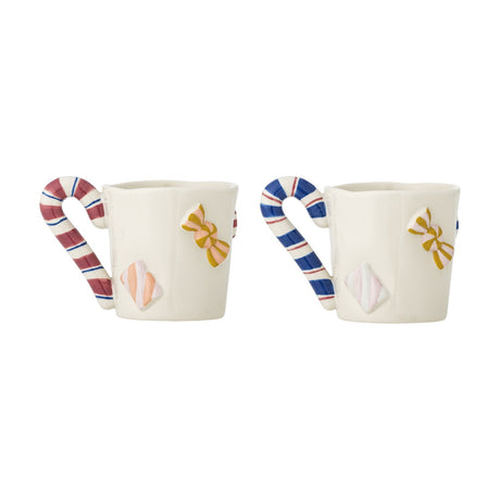 Set of two white stoneware Christmas mugs with candy cane-shaped handles in red and blue stripes, embossed sides decorated with hand-painted bows and sweets, on a plain white background.