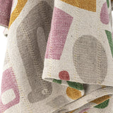 Close-up of the Filur Cotton Throw in multicoloured abstract shapes, showing woven fabric texture in mustard, pink, green and grey tones.