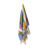 Artista Cotton Throw in Multi, a cotton blend throw with abstract multicoloured block stripes and knotted fringe tassels, shown hanging against a plain white background.