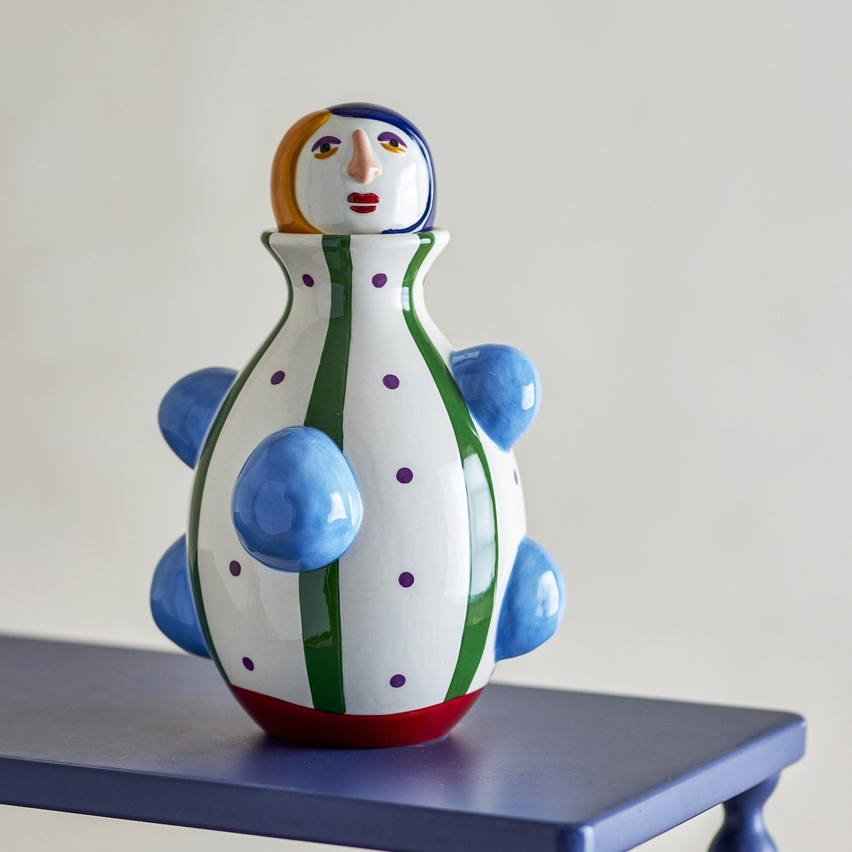Conneli Ceramic Vase 33cm - figure-shaped dolomite vase with painted face, striped and polka-dot body, blue knob details, and red base, shown on a blue table.