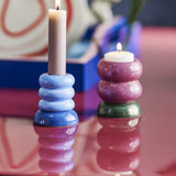 Tana Speckled Tealight & Candle Holders Set of 2 in stoneware, a blue ribbed candle holder with lit taper and a pink stacked tealight holder on green base, shown lit on a reflective pink surface.
