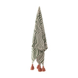 Woodsby Striped Cotton Throw hanging against a white background, showing a wavy green and cream striped pattern with pink tassels at each corner.