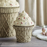 Cillie 41cm Natural seagrass basket with lid, ice-cream cone shape, criss-cross woven base, domed swirl lid with yarn sprinkles, shown beside a larger matching basket in a nursery.