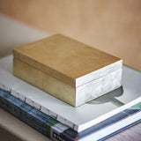 Nenon Storage Box with Lid in gold-toned MDF with a glossy finish, rectangular shape with fitted lid, shown atop stacked books in a living room setting.
