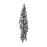 Santena Wavy Cotton Throw in blue, draped with fringed edges, showing a woven wave and dotted circle pattern in navy and beige against a plain white background.
