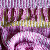 Isnel Striped Throw in pink, close-up of the textured woven fabric with striped bands in pink, mustard and white, finished with knotted fringe tassels.
