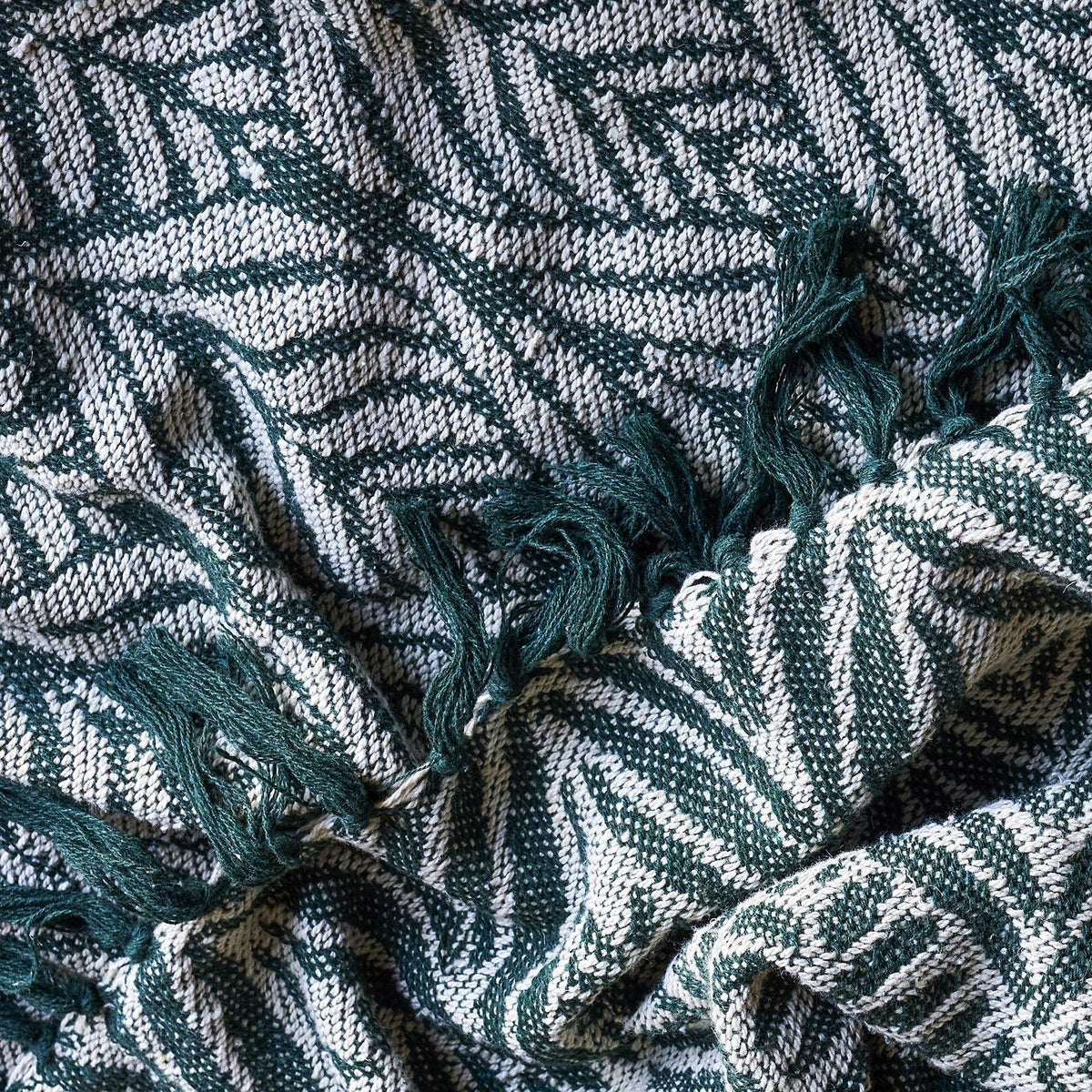 Ugento Leaf Cotton Throw in green, close-up of woven fern leaf pattern with knotted fringe edge, showing soft draped cotton fabric texture.