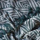 Ugento Leaf Cotton Throw in green, close-up of woven fern leaf pattern with knotted fringe edge, showing soft draped cotton fabric texture.