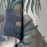 Peacock Throw in green, close-up of folded woven fabric showing palm fronds, leaves and stone shapes in muted green, grey and blue tones.