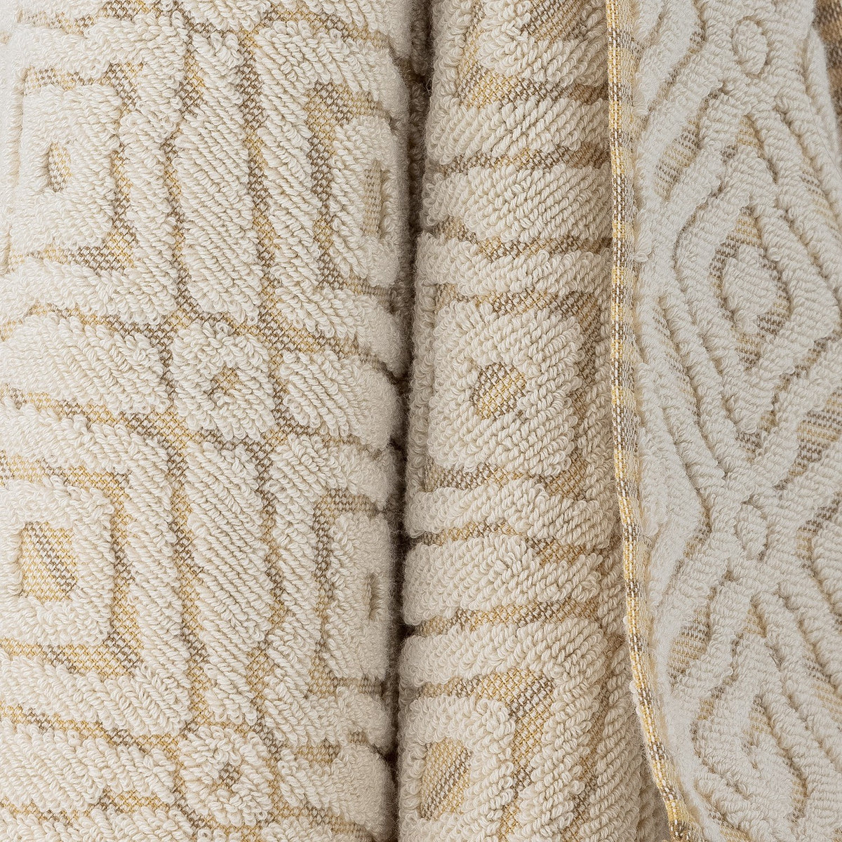 Close-up of the Malou Cotton Towel in natural, showing a raised geometric diamond and square pattern in looped pile against a flat woven ground, with a gold-striped edge trim.