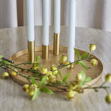 Maxime Iron Christmas Candle Holders Set of 7 in gold, round textured tray with four slim tube holders holding white taper candles, styled with green berry foliage on a marble table.