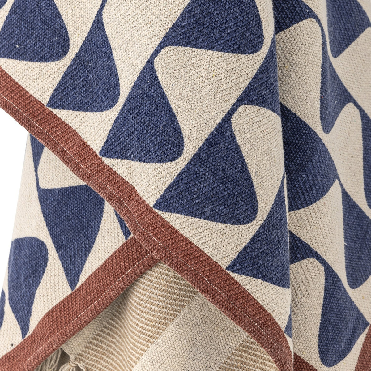 Rimme Cotton Throw in Multi, close-up of navy wave-pattern print with rust-brown edge border, cotton fabric draped to reveal a woven stripe reverse side.