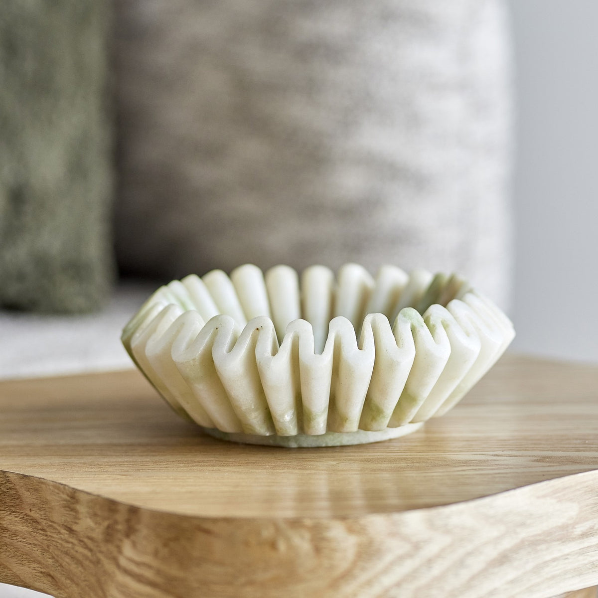 Harmonia Fluted Marble Bowl 17.5cm in white with a deep ruffled, wavy rim, shown on a wooden table against a softly blurred neutral room setting.