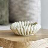 Harmonia Fluted Marble Bowl 17.5cm in white with a deep ruffled, wavy rim, shown on a wooden table against a softly blurred neutral room setting.