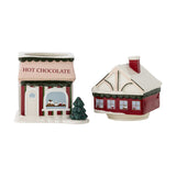 Gloria Ceramic Christmas Storage Jar 2500ml in red, shaped as a "Hot Chocolate" shop with a snow-topped lift-off roof lid, shown beside a matching house-shaped jar on a white background.