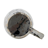 Top-down view of a Winnie stoneware mug with handle, showing its multicoloured reactive glaze splashes and speckles inside and around the rim, on a plain white background.
